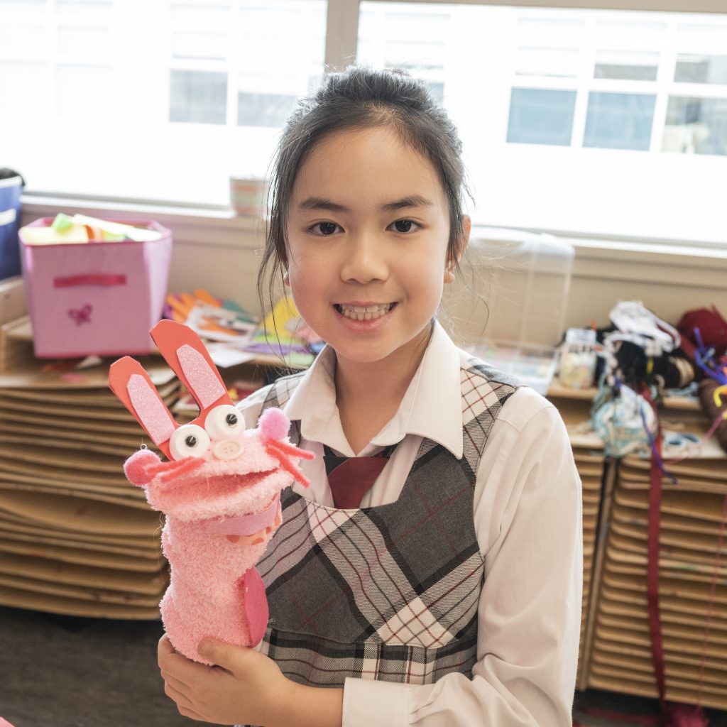 A Junior School student holding up a hand puppet and smiling